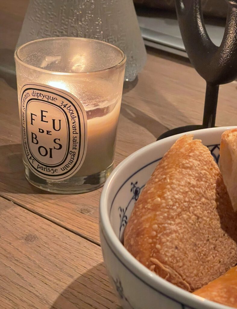 Tent lys ved siden av en skål med bakverk på et trebord.